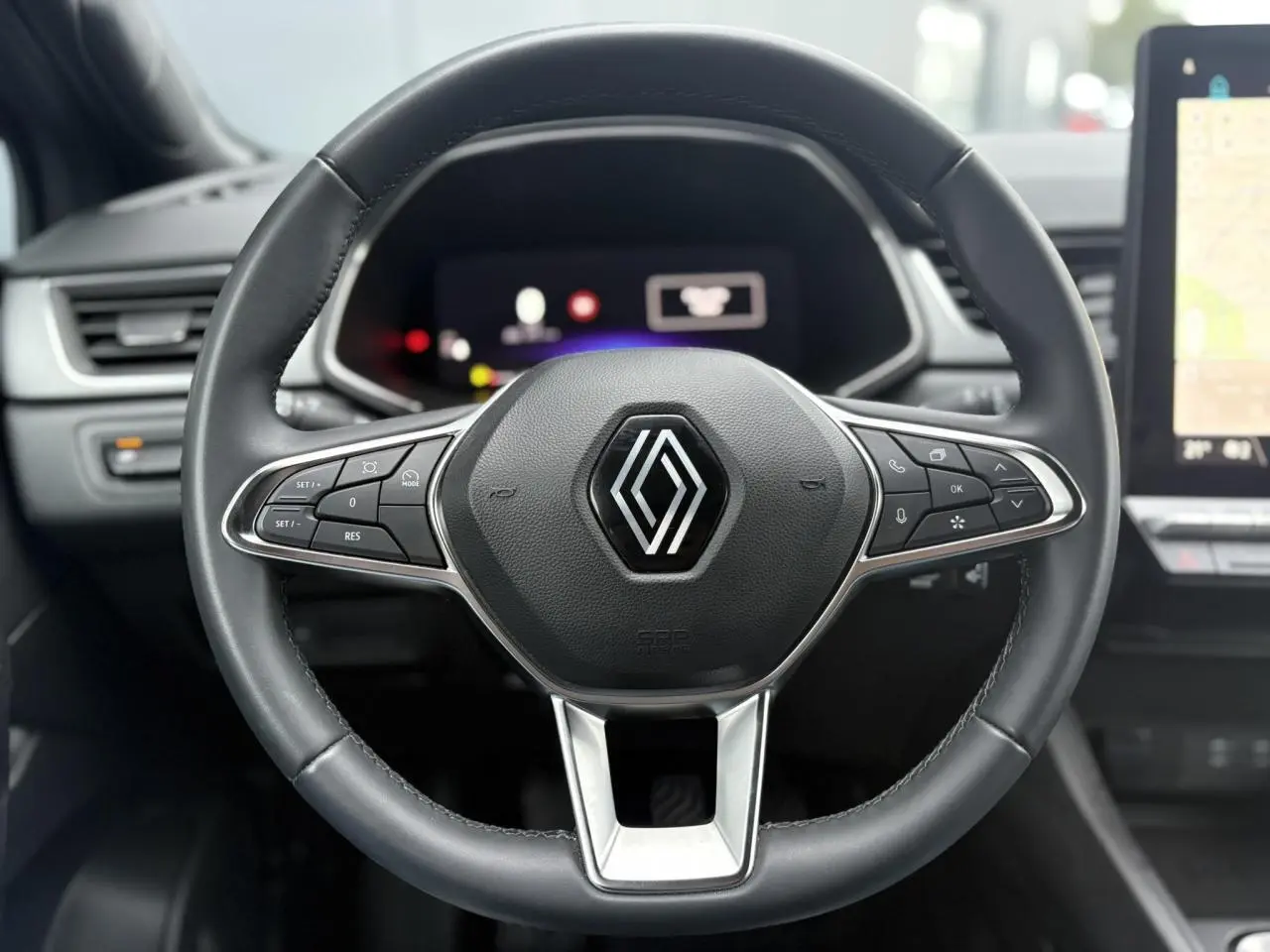 Vue rapprochée du volant cuir noir du Renault Captur 2025 avec commandes intégrées et tableau de bord numérique flou.