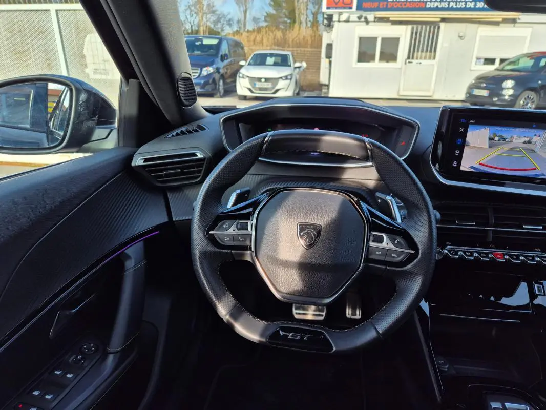 Vue intérieure centrée sur le volant noir GT du Peugeot 2008 Hybrid 145 avec écran tactile affichant la caméra de recul.