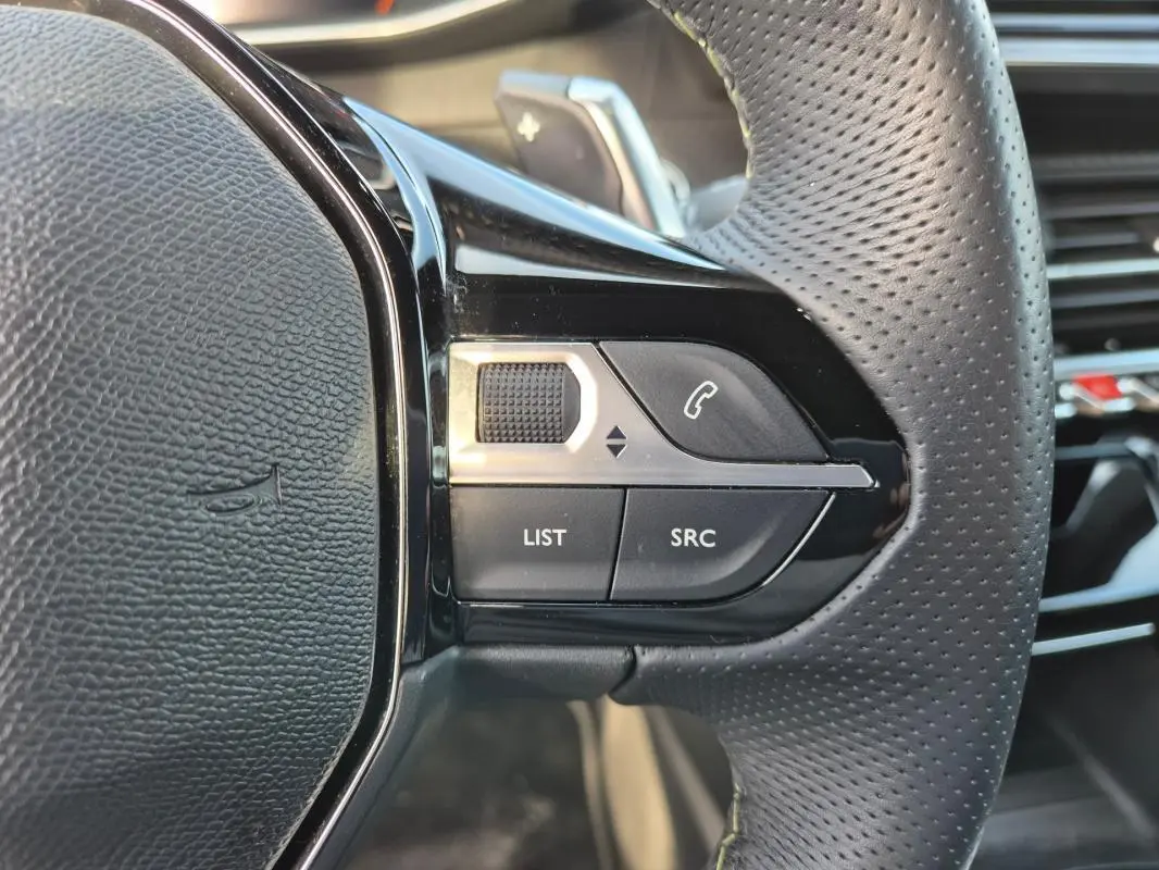 Gros plan sur la partie droite du volant noir perforé du Peugeot 2008 Hybrid 145 e-DCS6 GT 2024, avec commandes intégrées.