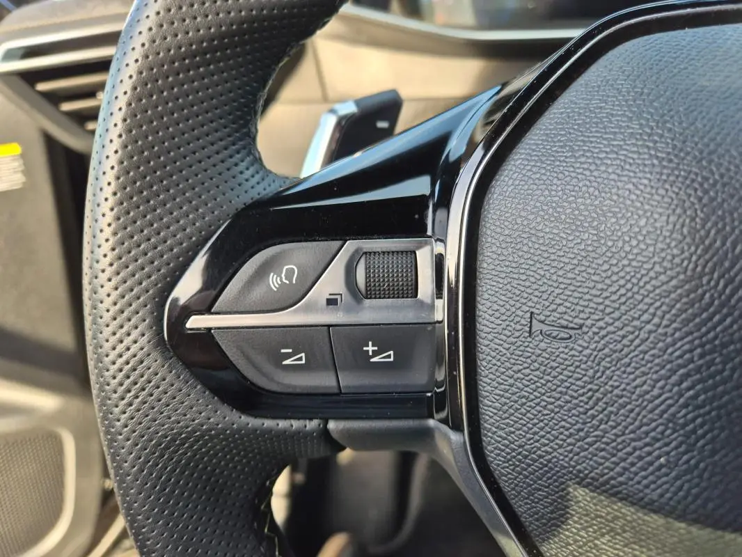 Gros plan sur les commandes gauche du volant noir perforé du Peugeot 2008 Hybrid 145 e-DCS6 GT 2024.