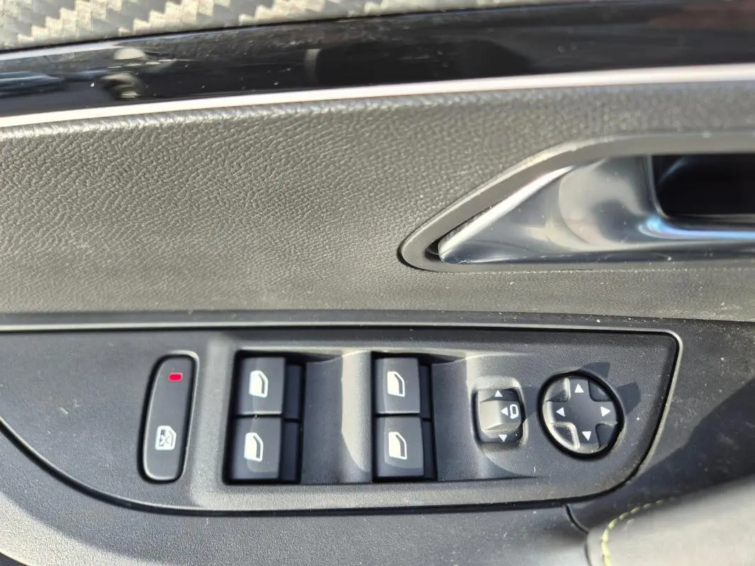 Gros plan sur les commandes de lève-vitres et réglage des rétroviseurs côté conducteur d'une Peugeot 2008 Hybrid 145 e-DCS6 GT noire.