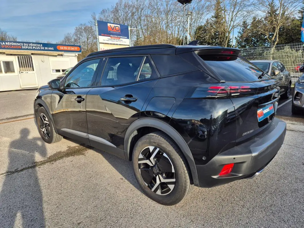Vue 3/4 arrière droite d'un Peugeot 2008 Hybrid 145 noir avec jantes alliage 18 pouces et barres de toit visibles.