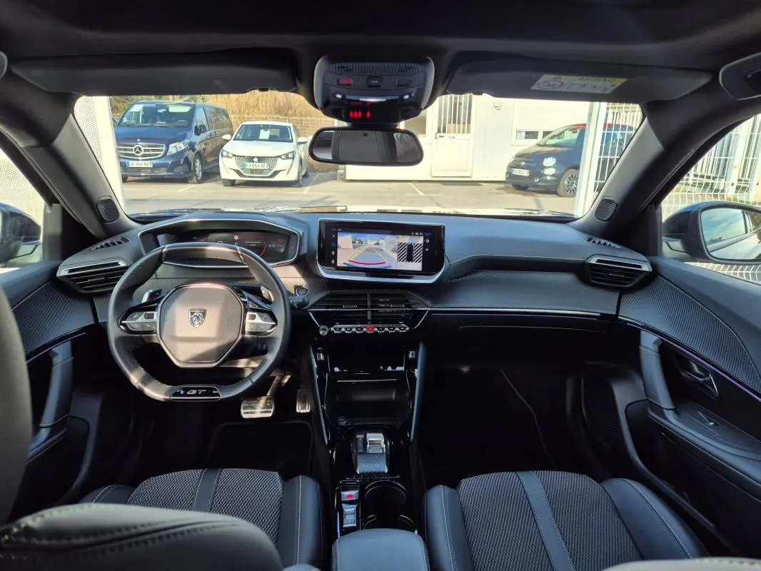 Vue intérieure avant du Peugeot 2008 Hybrid 145 e-DCS6 GT noir, avec tableau de bord numérique et écran tactile central affichant la caméra de recul.