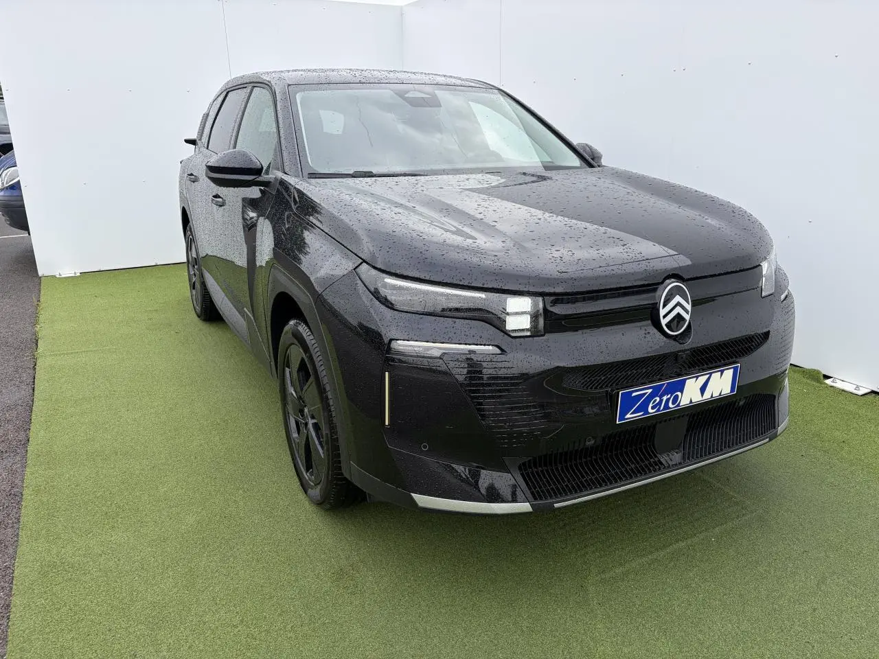 Citroën C5 Aircross noir métal en 3/4 avant droit, avec pluie visible sur la carrosserie et jantes noires.