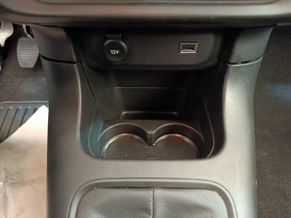 Gros plan de la console centrale noire avec prise 12V, port USB et porte-gobelets dans une Citroën C3 blanche.