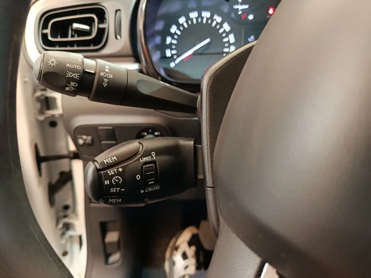 Gros plan sur la commande de régulateur de vitesse à gauche du volant dans l’habitacle d’une Citroën C3 blanche.
