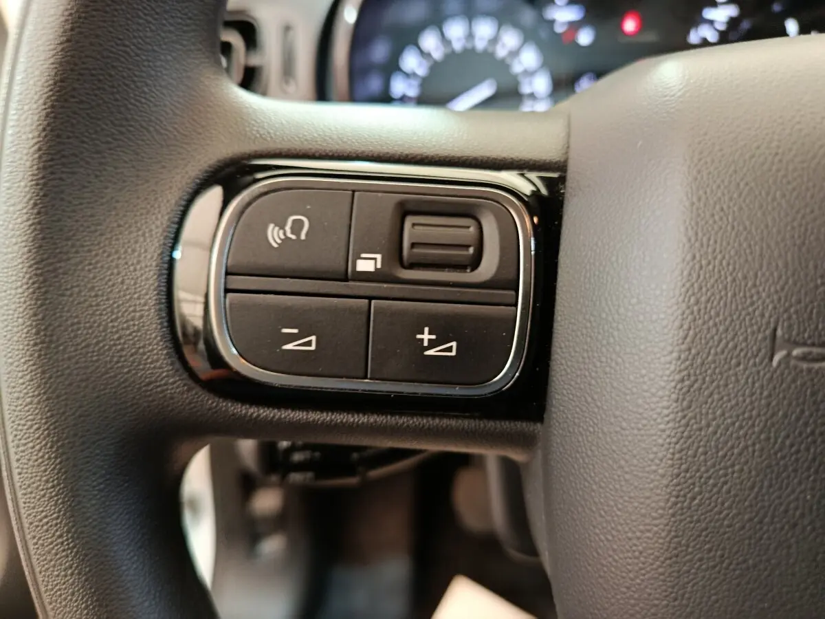 Gros plan sur les commandes multifonctions du volant noir d'une Citroën C3 blanche, version PureTech 83 2020.