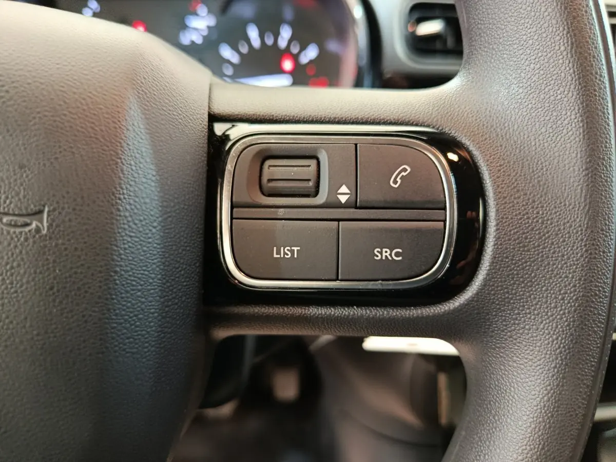 Gros plan sur les commandes multifonctions noires du volant de la Citroën C3 blanche, côté gauche.