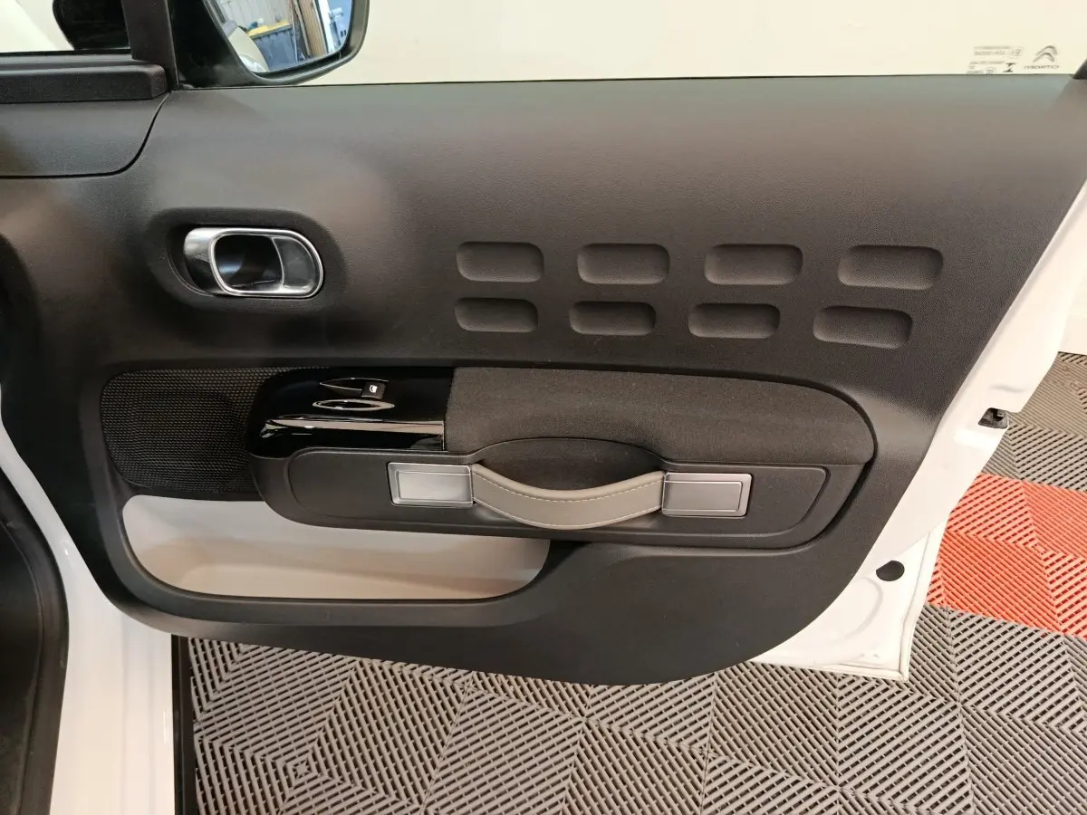 Vue intérieure du panneau de porte avant gauche blanc de la Citroën C3 avec poignée beige et commandes de vitres noires.