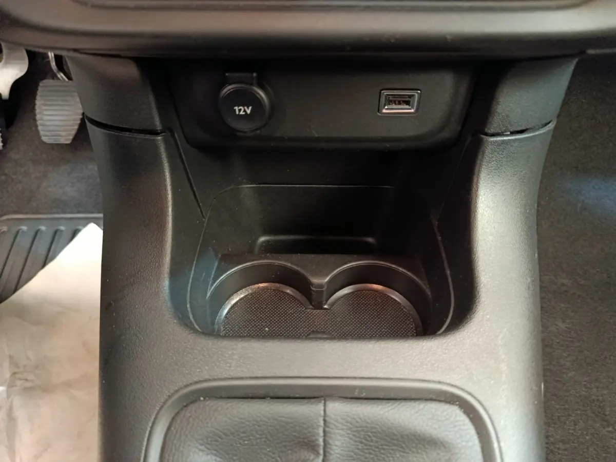 Gros plan sur la console centrale noire de la Citroën C3, montrant porte-gobelets, prise 12V et port USB.