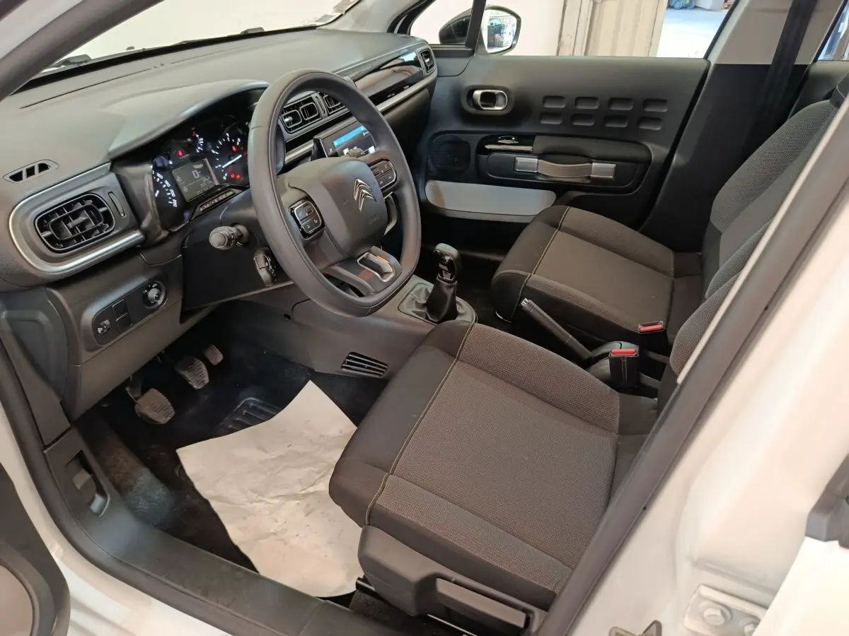 Intérieur de la Citroën C3 blanc, vue côté conducteur, montrant tableau de bord, volant multifonctions et sièges noirs.