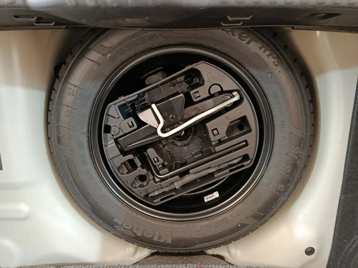 Gros plan sur la roue de secours noire avec kit de réparation intégré dans le coffre d'une Citroën C3 blanche.