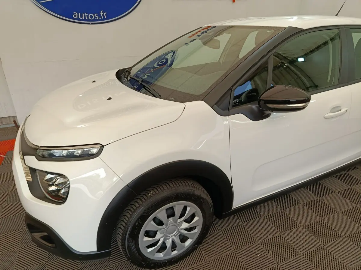Vue 3/4 avant droit d'une Citroën C3 blanche avec rétroviseur noir et phares LED distinctifs.