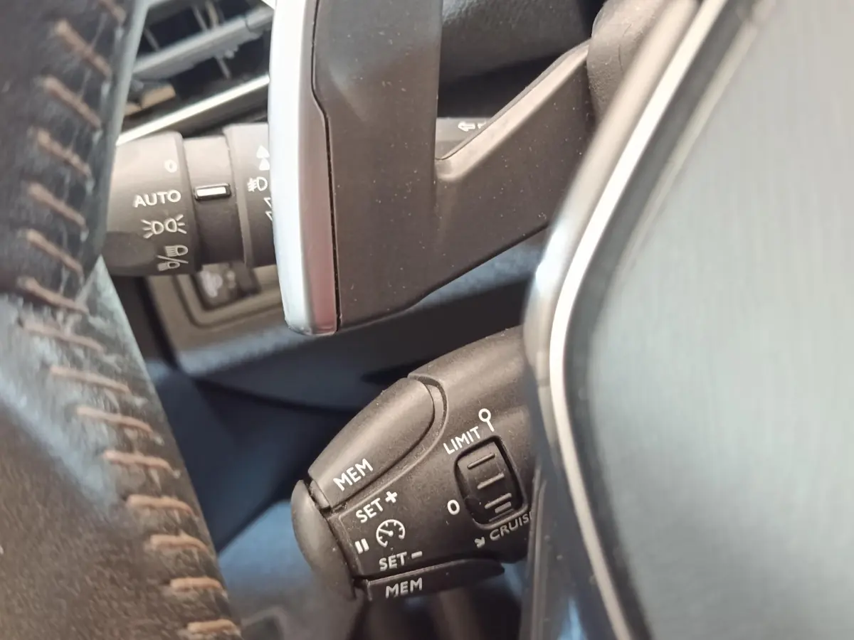 Gros plan sur la commande de régulateur de vitesse noire, vue côté gauche du volant cuir d’un Peugeot 5008 noir.
