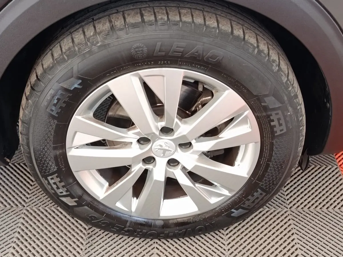 Gros plan sur la roue avant droite d’un Peugeot 5008 noir, avec jante alliage argentée et pneu LEAO.
