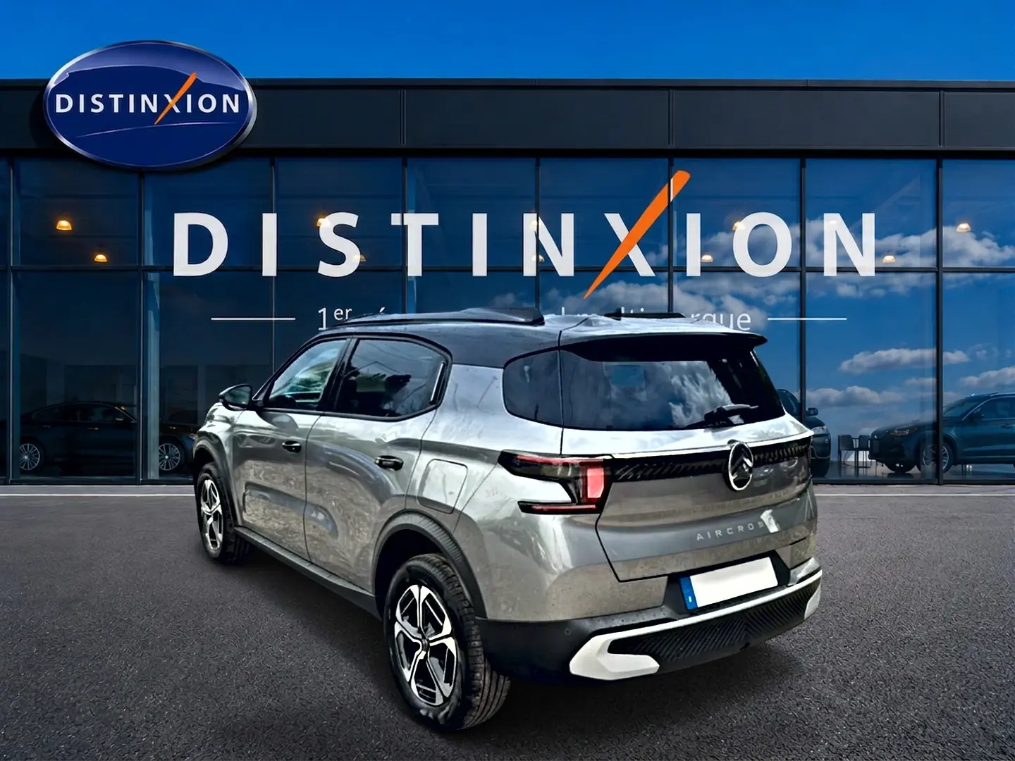 Vue 3/4 arrière droite d'un Citroën C3 Aircross gris mercury avec jantes alu et toit noir devant un showroom Distinxion.