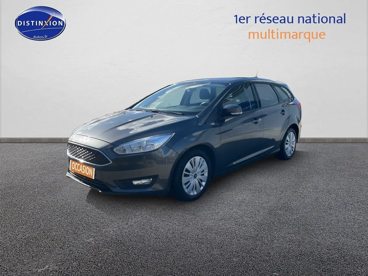 Ford Focus SW gris magnetic metal vue 3/4 avant droit sur sol bitumé avec plaque occasion orange visible