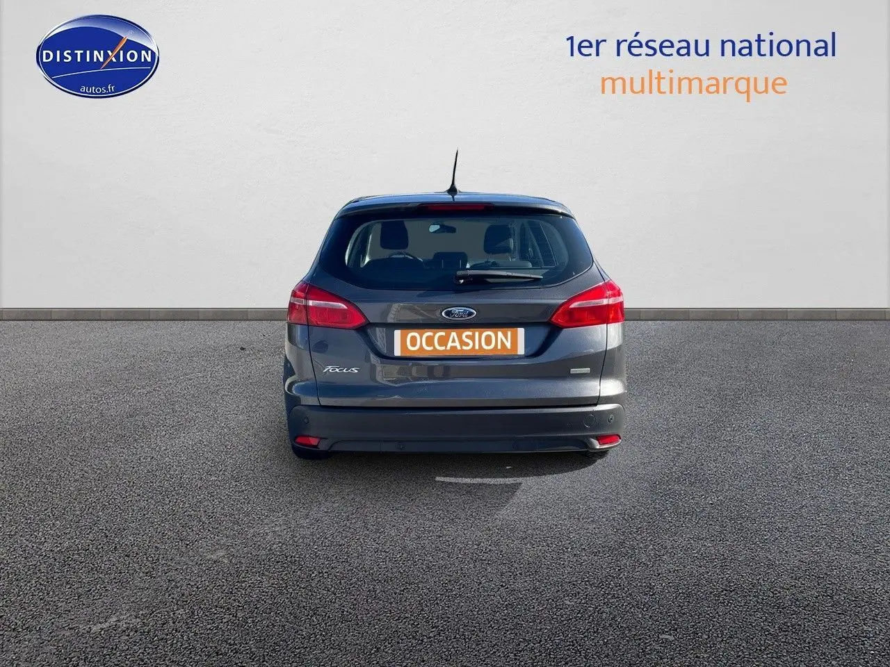 Vue arrière d'une Ford Focus SW gris magnetic metal avec plaque orange "OCCASION" sur un sol goudronné.