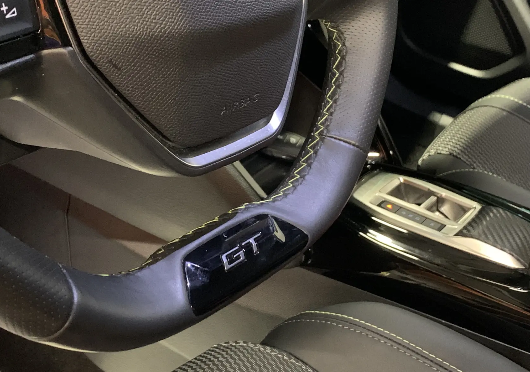Gros plan sur le volant GT avec surpiqûres jaunes du Peugeot 2008 gris, intérieur cuir et détails carbone visibles.
