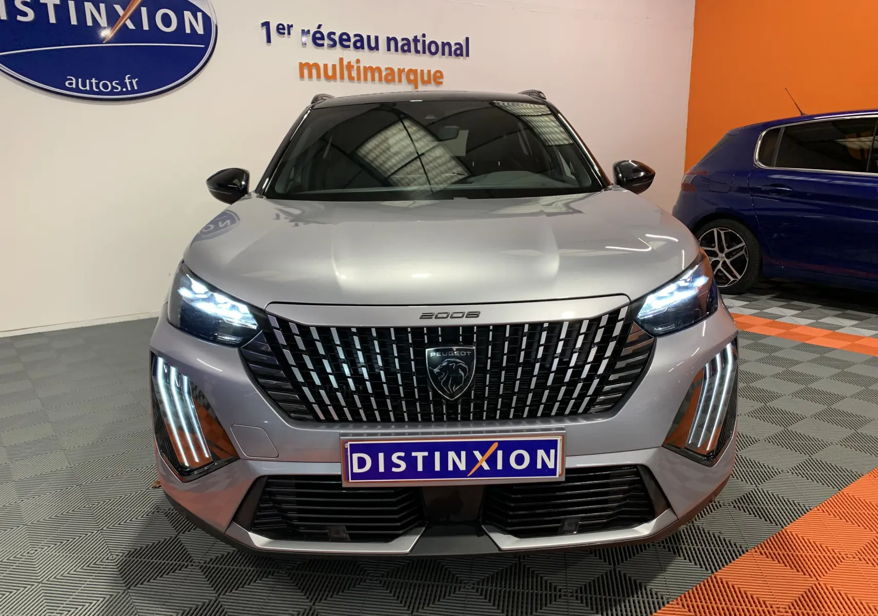Vue frontale d'un Peugeot 2008 gris 2023 avec calandre noire et feux LED allumés en intérieur showroom