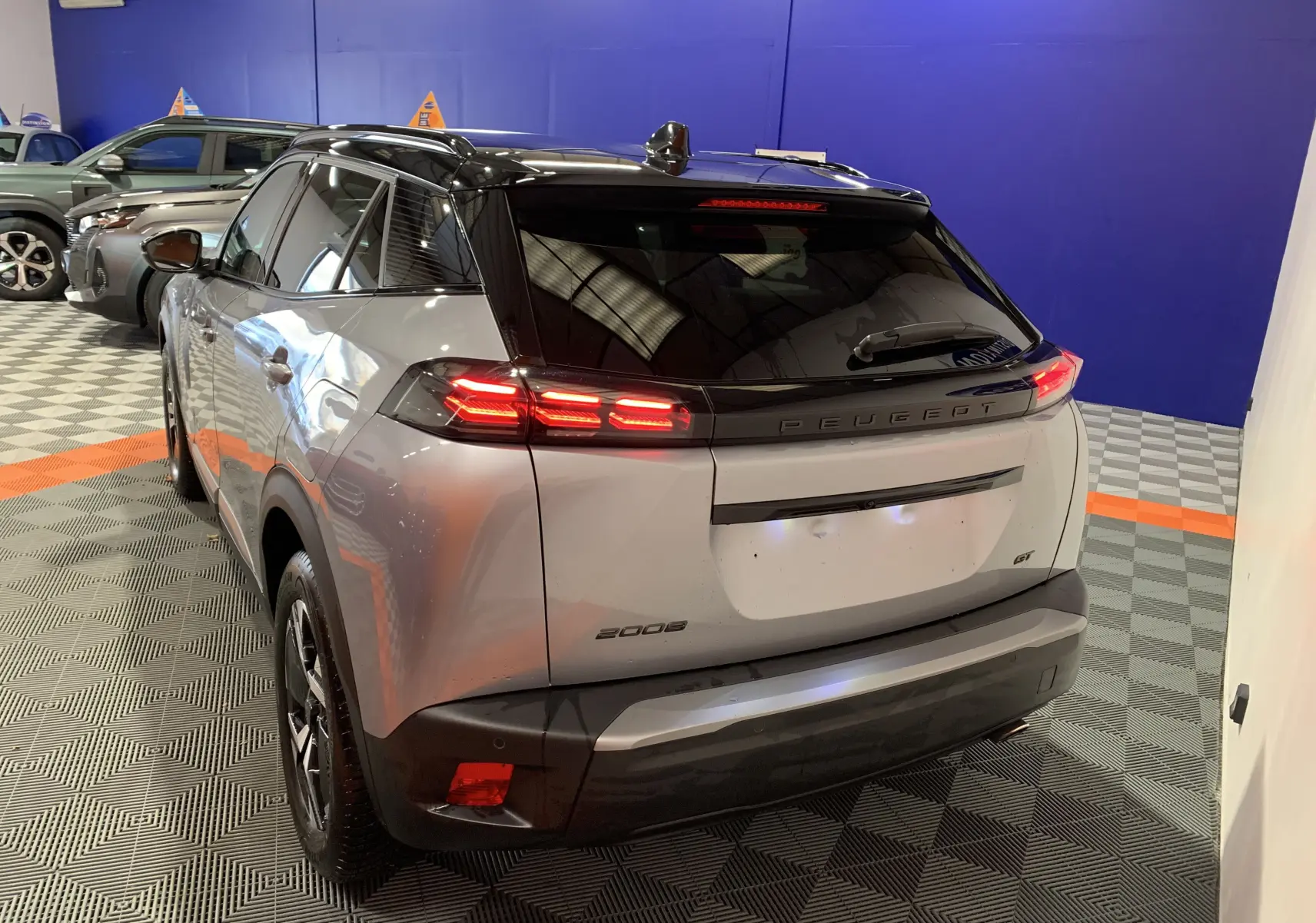 Vue 3/4 arrière droite d'un Peugeot 2008 gris 2023 avec feux LED allumés et toit noir dans un showroom.