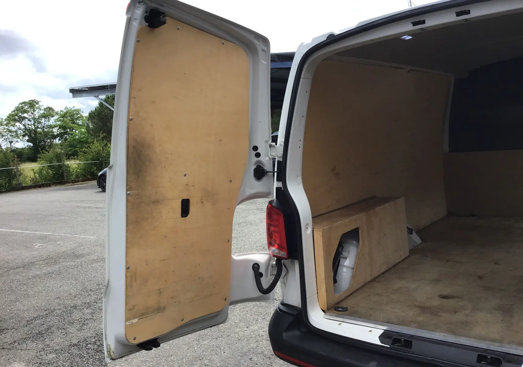 Vue arrière ouverte côté gauche d'un Volkswagen Transporter 6.1 blanc, montrant l'intérieur utilitaire en bois.