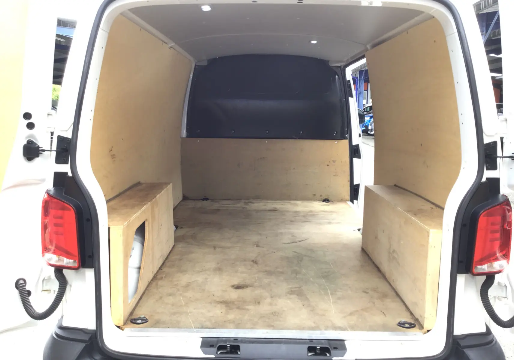 Vue arrière du Volkswagen Transporter 6.1 blanc, montrant l'espace de chargement avec aménagements en bois sur les côtés.
