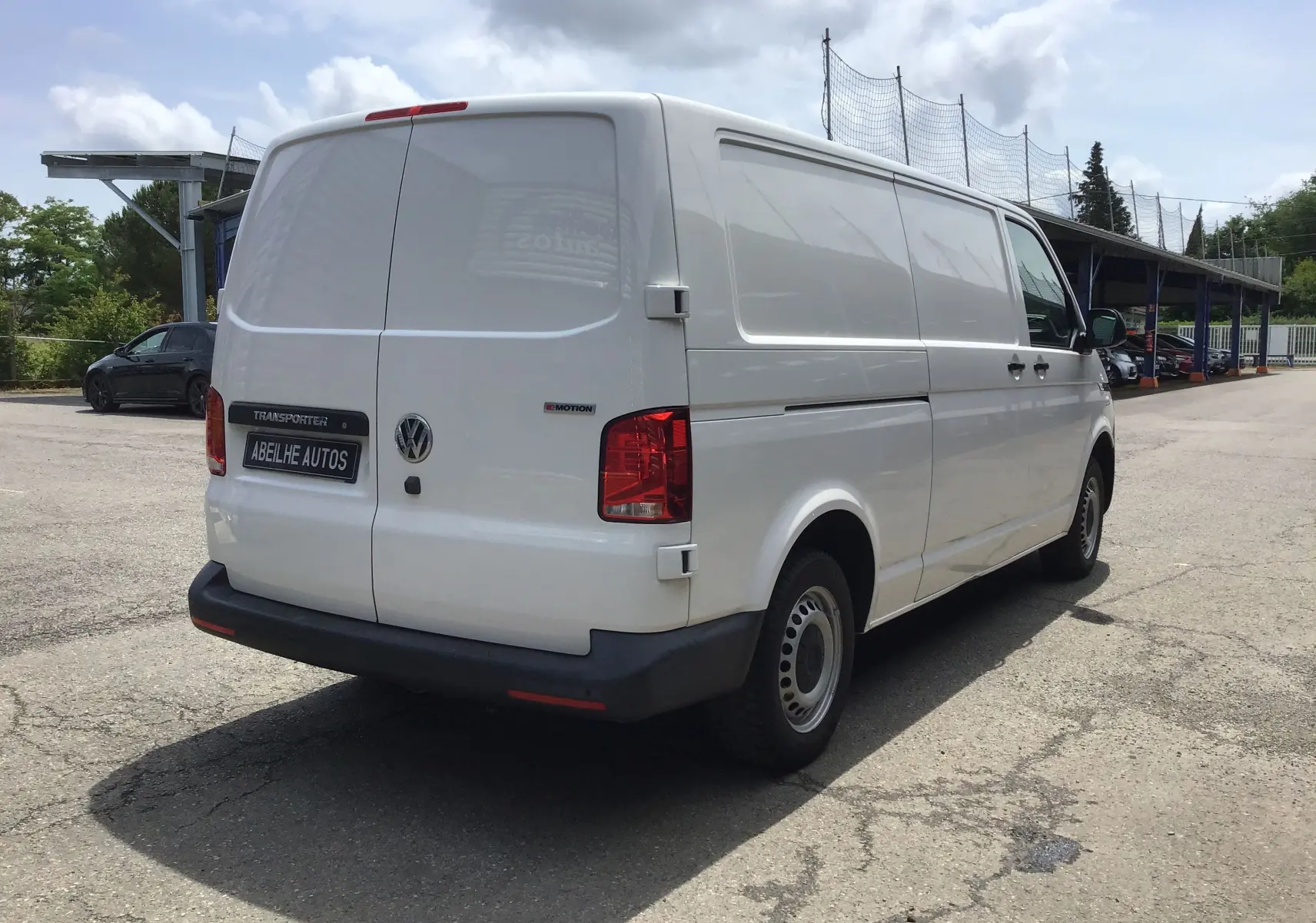 Vue 3/4 arrière droite d’un Volkswagen Transporter 6.1 blanc, fourgon utilitaire avec logo 4MOTION et plaque Abeilhe Autos.