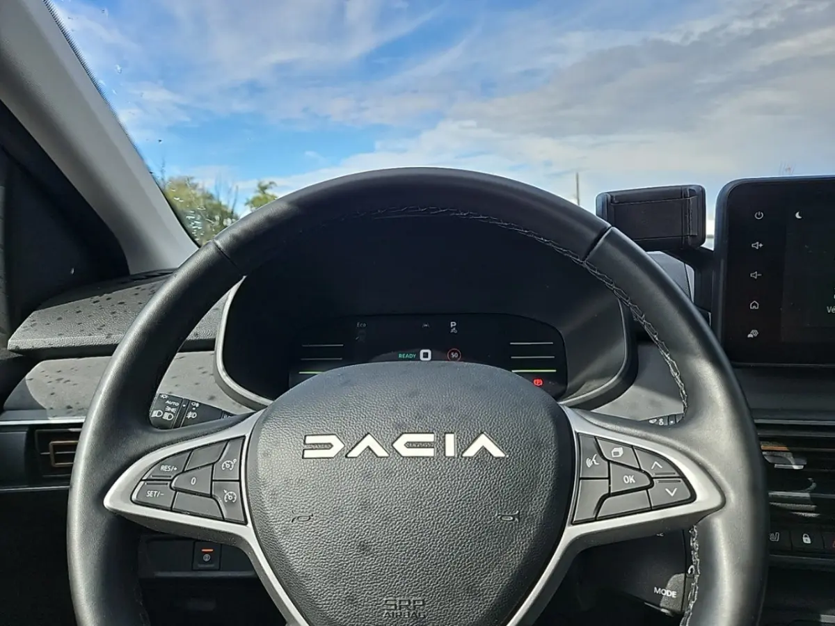 Volant noir avec logo DACIA en gros plan, tableau de bord digital et écran tactile visible à droite, intérieur du Jogger 2024.