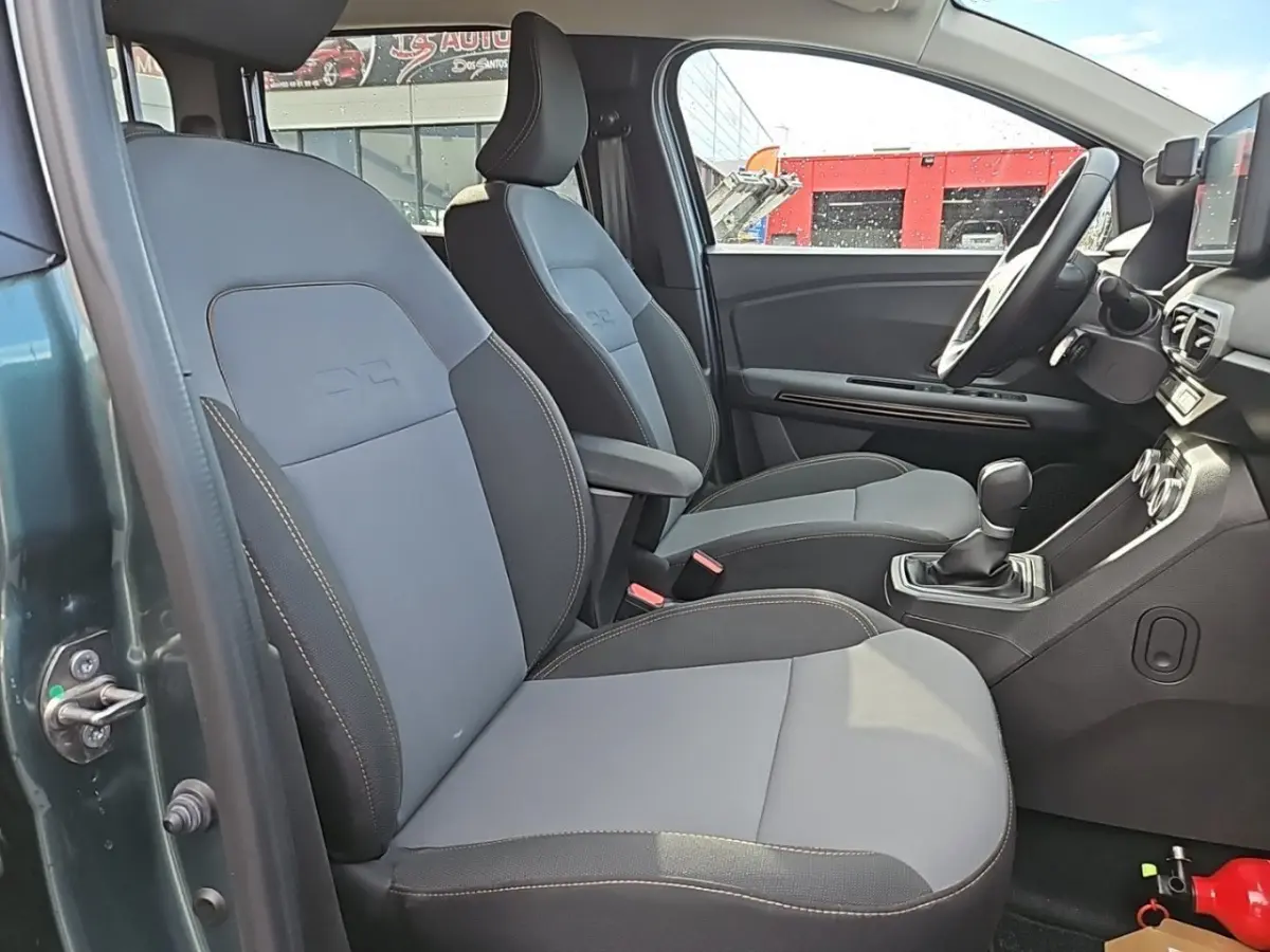 Vue intérieure côté conducteur du Dacia Jogger vert 2024, sièges avant gris avec surpiqûres contrastées et volant multifonctions.