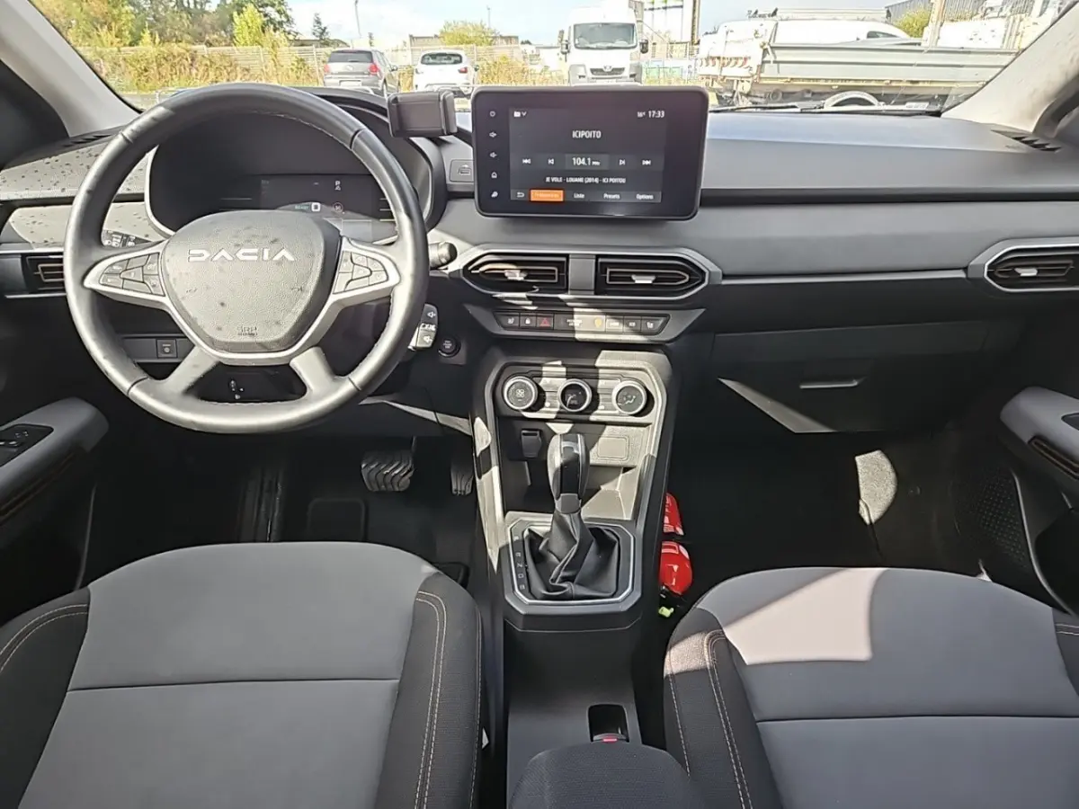 Vue intérieure avant du tableau de bord et volant DACIA Jogger avec écran tactile central et sièges gris.