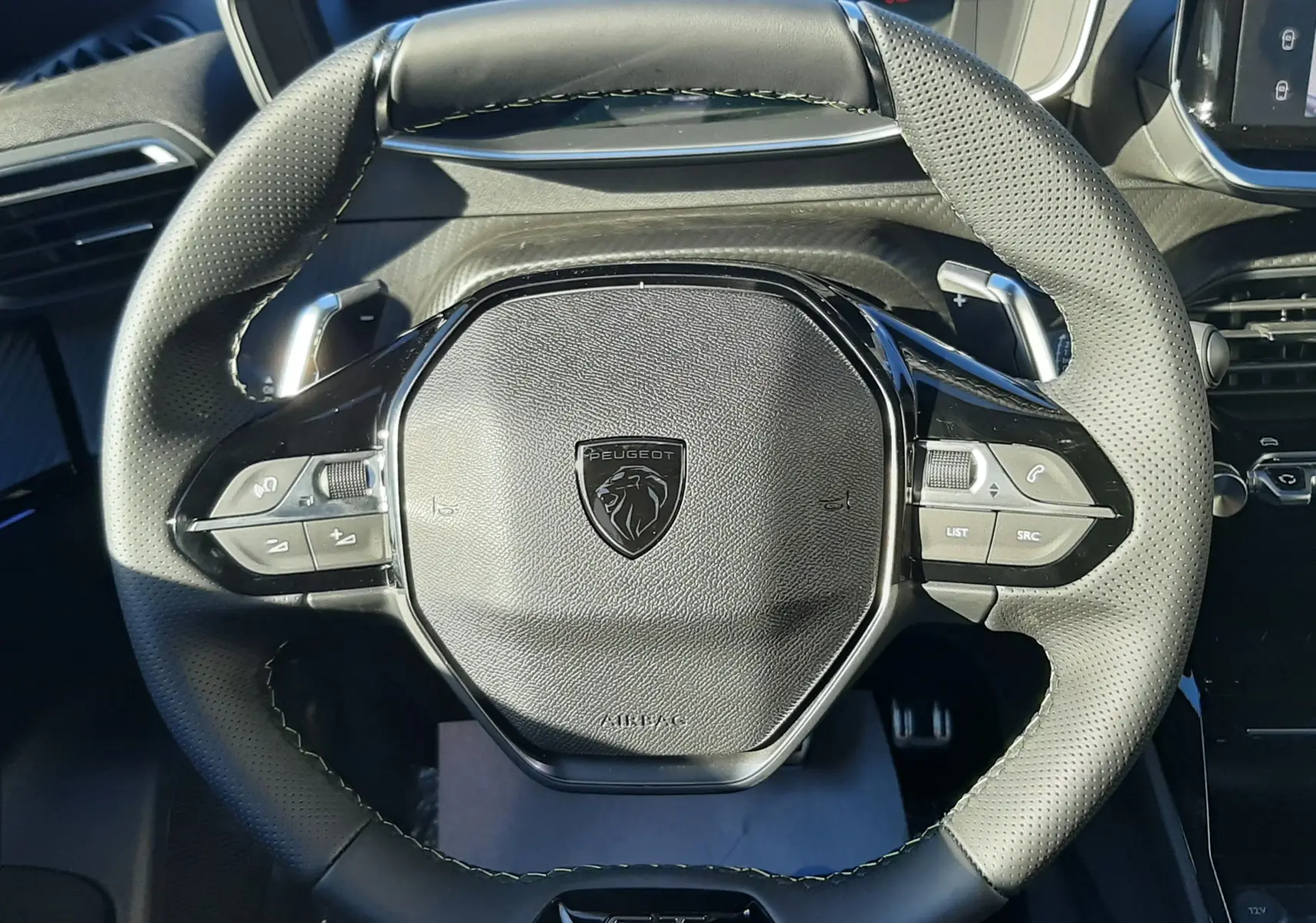 Gros plan sur le volant cuir perforé noir avec logo Peugeot et badge GT du Peugeot 2008 gris Selenium 2025 hybride.