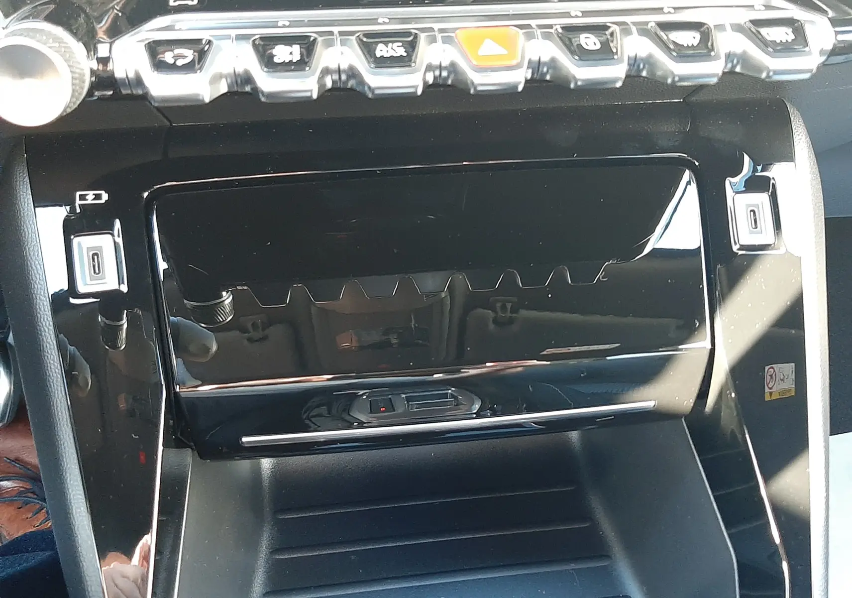 Vue rapprochée de la console centrale noire brillante du Peugeot 2008 gris Selenium, avec boutons de commande et prise 12V visibles.