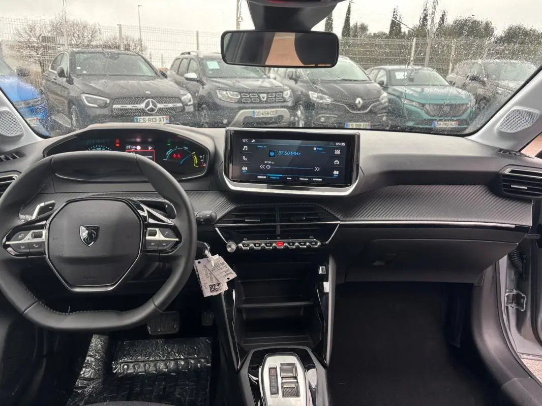 Vue intérieure avant du tableau de bord gris de la Peugeot 208 Hybrid 100 e-DCS6 avec écran tactile et volant multifonction.