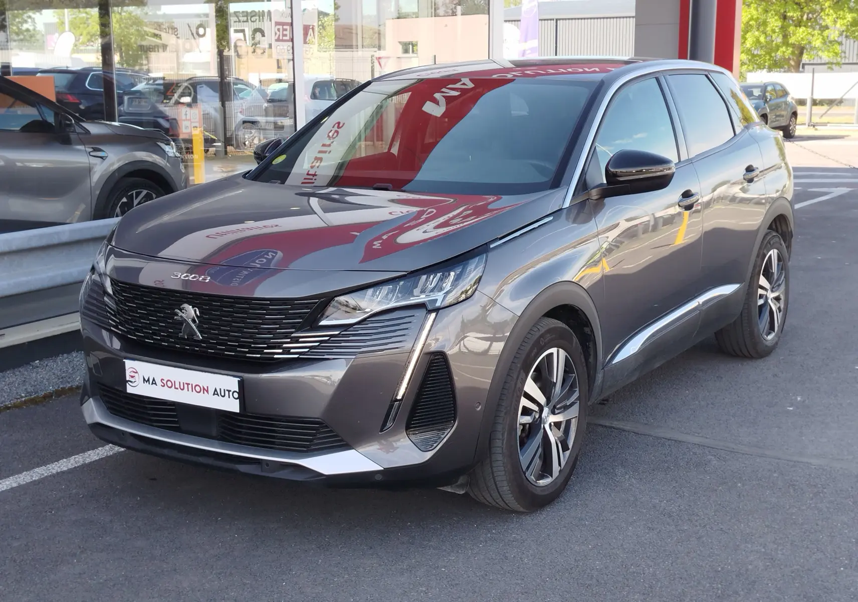 Peugeot 3008 gris Platinium en 3/4 avant droit, avec calandre noire et feux LED distinctifs, stationné devant un showroom.