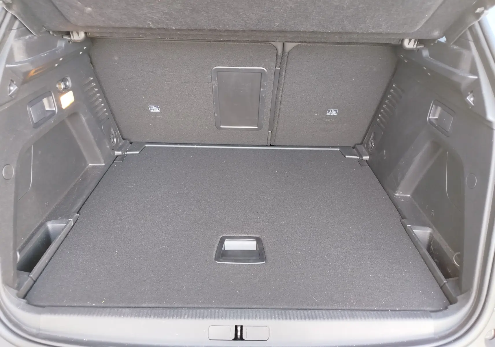Vue intérieure du coffre spacieux et propre du Peugeot 3008 gris Platinium, avec banquette arrière rabattue partiellement.
