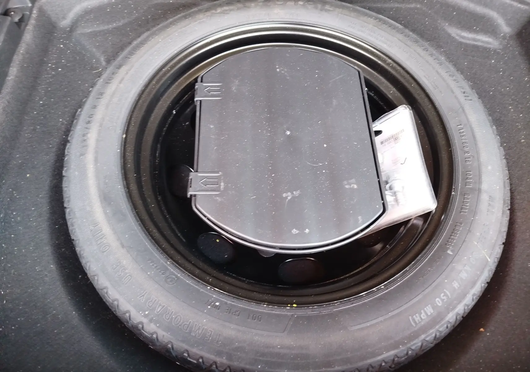 Vue plongeante sur la roue de secours noire et son kit de réparation dans le coffre du Peugeot 3008 Gris Platinium 2023.