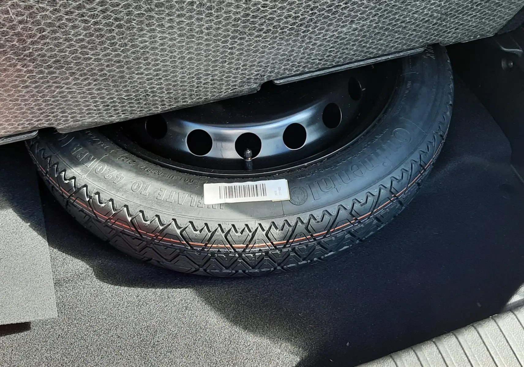 Pneu de secours noir avec jante acier visible sous la moquette du coffre d’un Renault Symbioz gris Rafale.