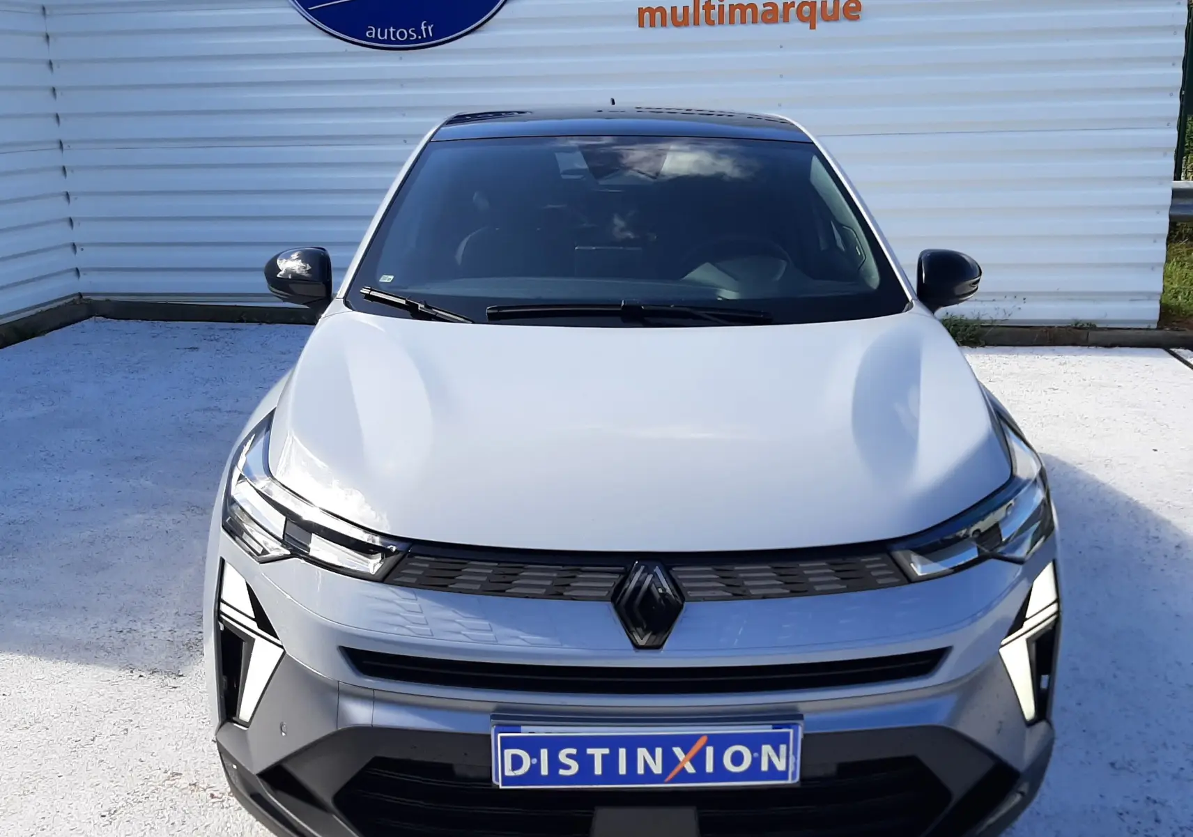 Vue avant d'une Renault Symbioz gris rafale avec calandre noire et phares LED, stationnée devant un mur blanc.