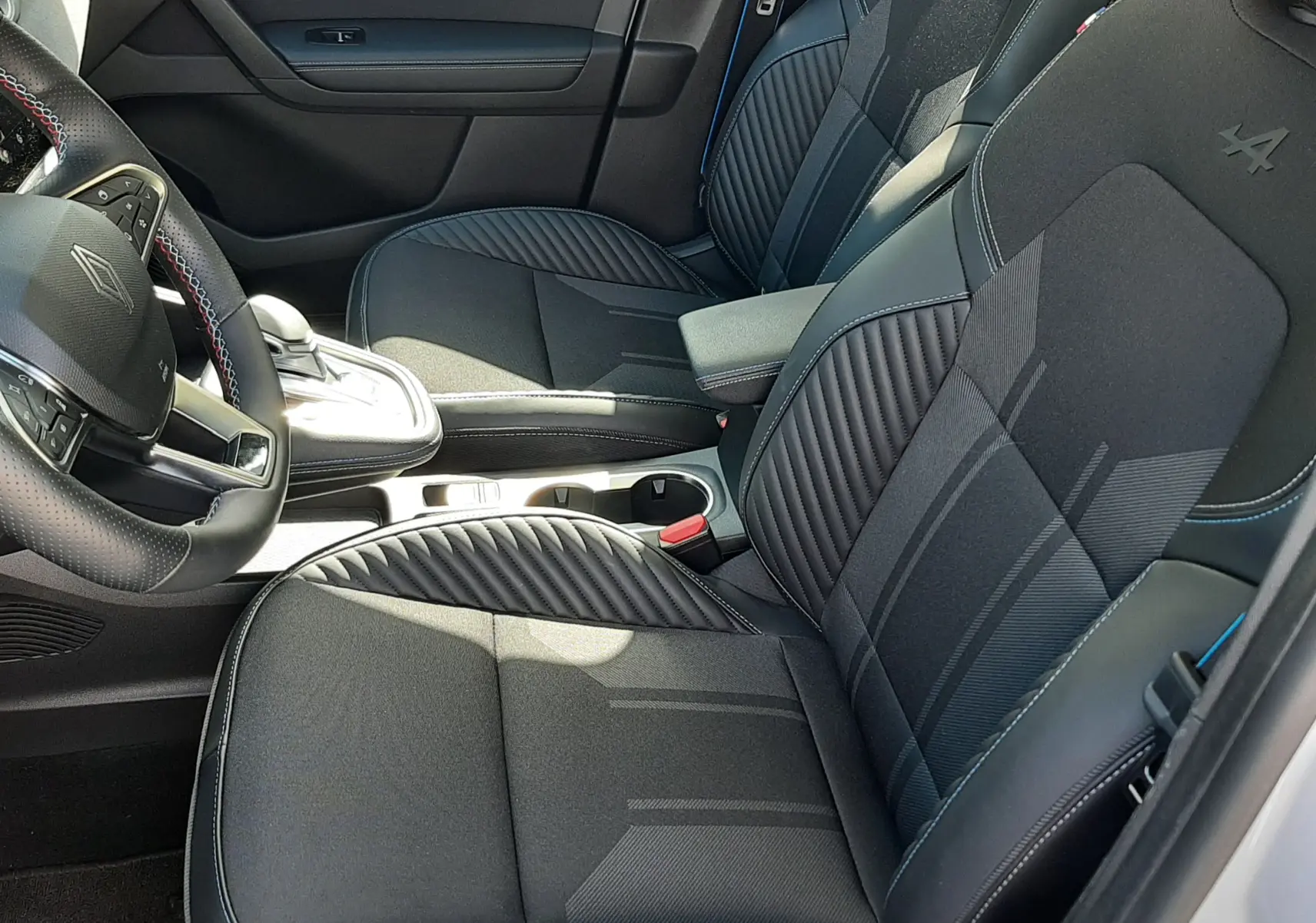 Vue intérieure côté conducteur de la Renault Symbioz E-Tech Full Hybrid 145 Esprit Alpine, sièges noirs avec surpiqûres bleues et logo Alpine brodé.