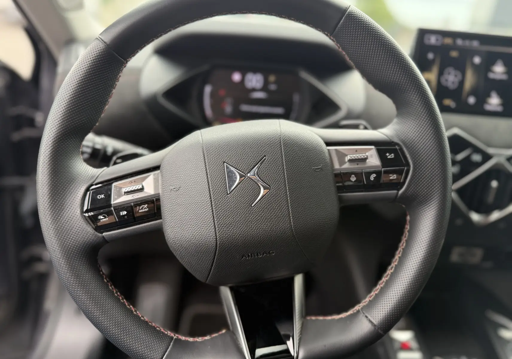Vue rapprochée du volant en cuir noir avec logo DS au centre, boutons multifonctions et coutures rouges visibles.