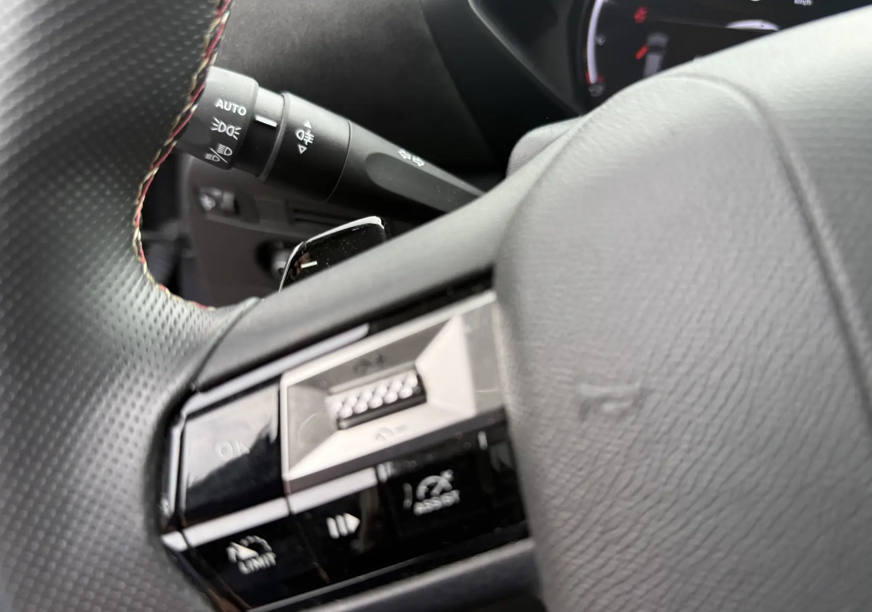 Gros plan sur la partie gauche du volant noir perforé du DS3 hybride 2025, avec commandes intégrées et levier de clignotant visible.