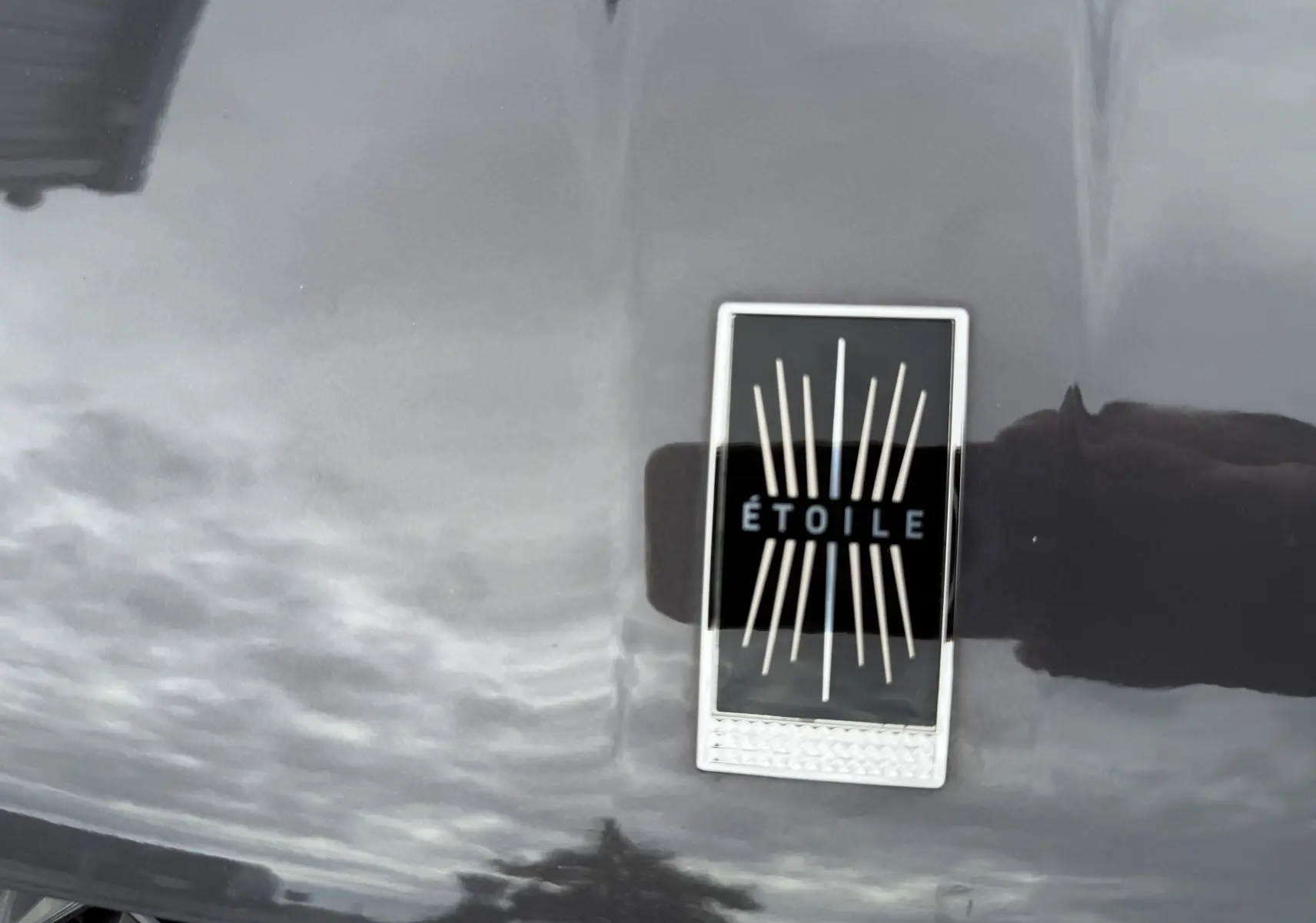 Gros plan sur l'écusson ÉTOILE noir et argent sur la carrosserie gris foncé du DS3 hybride 2025.