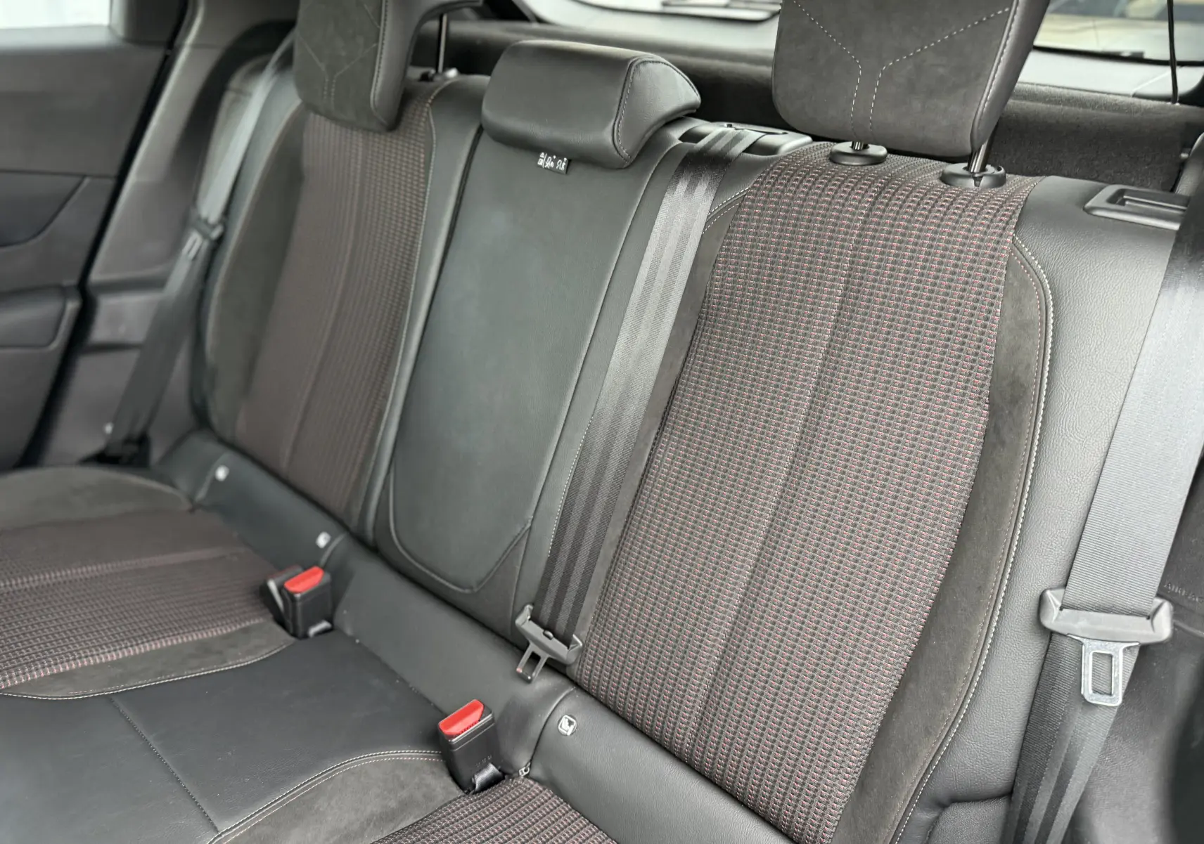 Vue rapprochée des sièges arrière du DS3 Hybride 2025, tissu à motif rouge et noir avec ceintures de sécurité visibles.