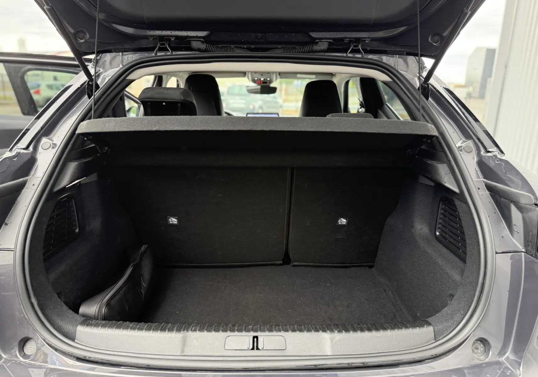 Vue arrière du coffre ouvert d'une DS3 hybride 2025 gris Vol de Nuit avec toit noir, montrant l'espace de chargement vide.