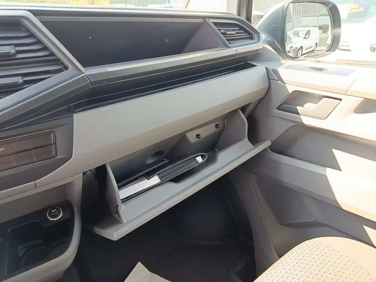 Intérieur côté passager du Volkswagen Transporter gris foncé 2022, avec boîte à gants ouverte et tableau de bord clair.