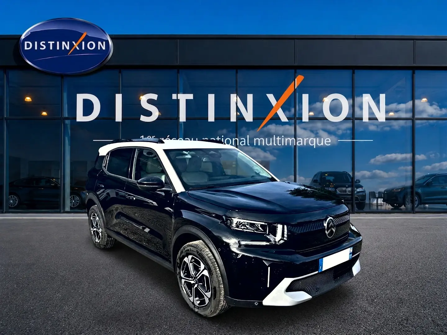 Vue 3/4 avant droite d'un Citroën C3 Aircross noir avec toit blanc, jantes alu et calandre moderne devant un showroom.