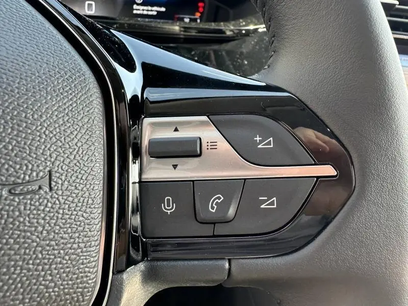 Gros plan sur les commandes multifonctions noires et argentées du volant de la Peugeot 308 bleu, côté gauche.