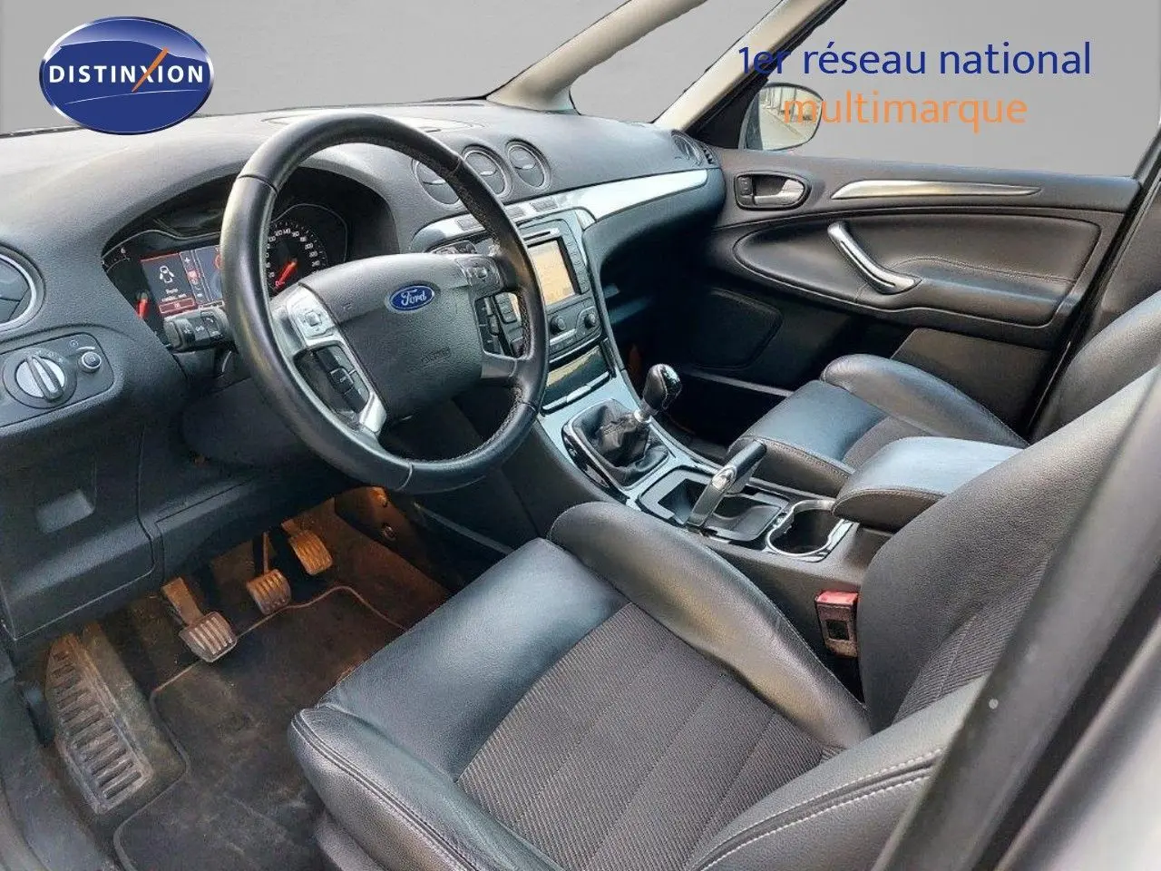 Intérieur du Ford S-MAX 2012 vu côté conducteur, volant cuir noir, tableau de bord avec écran GPS et boîte manuelle.