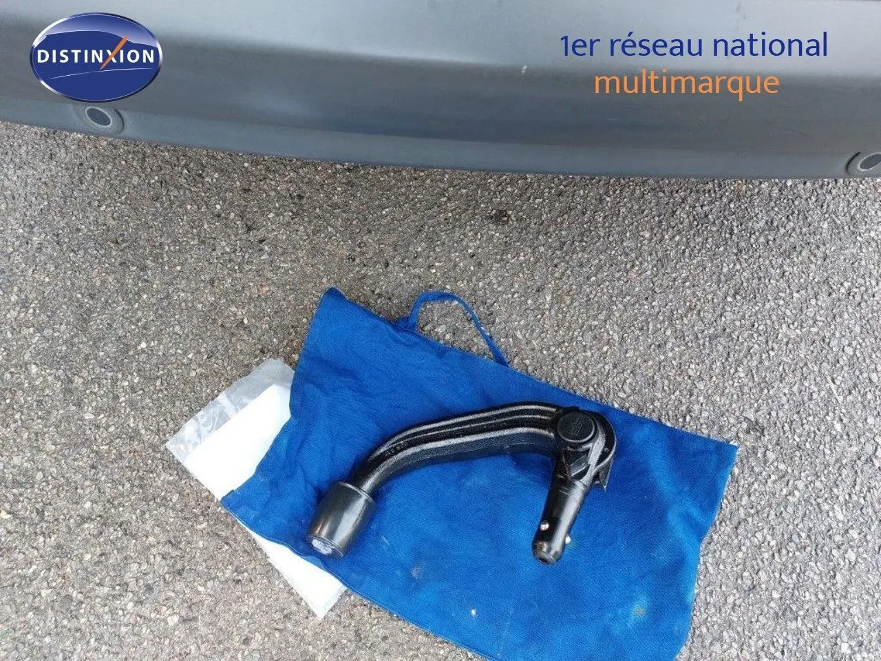 Gros plan sur l'attelage noir posé sur un sac bleu devant un Ford S-MAX gris clair métal, vue arrière basse.